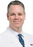 Dr. Brandon Valentine wears a white coat and smiles.