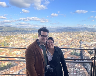 Dr. Ryan Hofler and his wife, Patty Ni, are standing at a high point with the large cityscape of Florence behind them.
