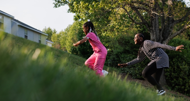 Kashinda Carter runs up a grassy hill with her daughter, Evelyn. 