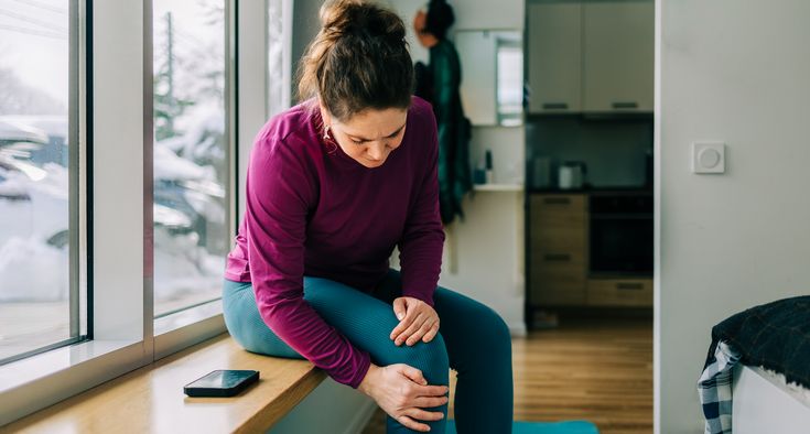 A woman is seated and grips her knee in discomfort.
