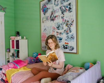 Ellie sits on her bed reading a book.