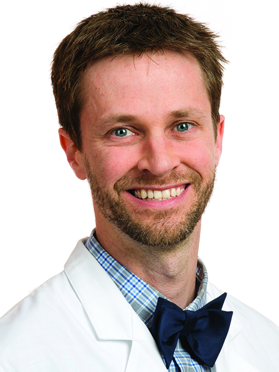 Dr. Joseph Chipman wears a white coat and a bowtie and smiles.