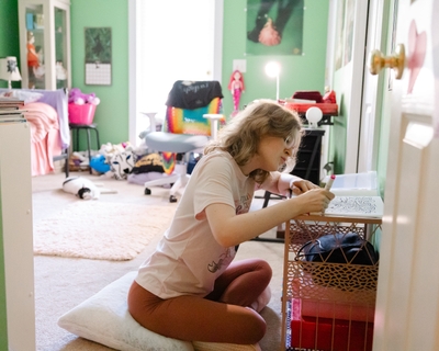 Ellie Strickland sits on the floor in her bedroom and colors with markers in a coloring book.