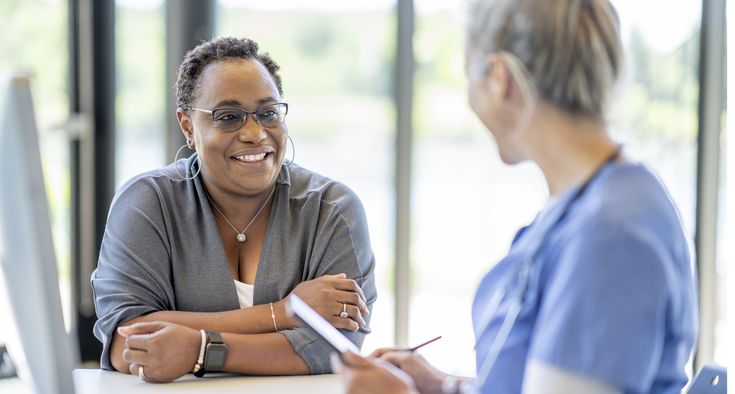 A woman and a nurse talk while sitting together at a table.