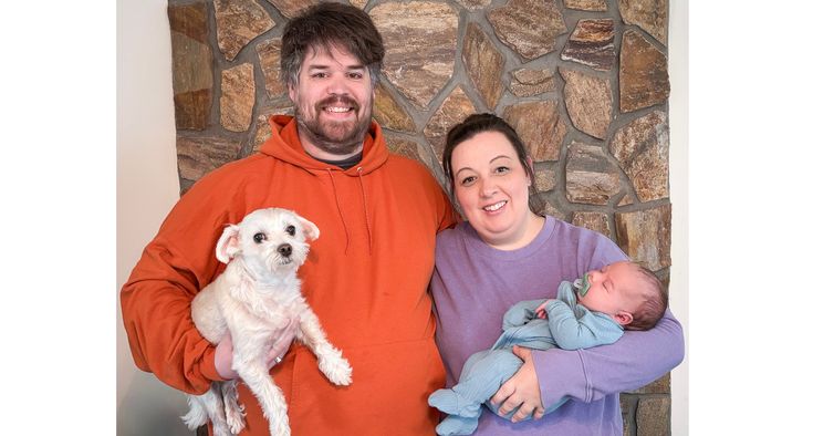Hunter and Lauren Miller stand together with their infant son, Carter, and their dog, Ollie.