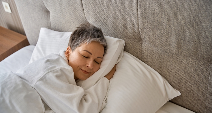  A woman with short hair sleeps on a bed with white sheets. 