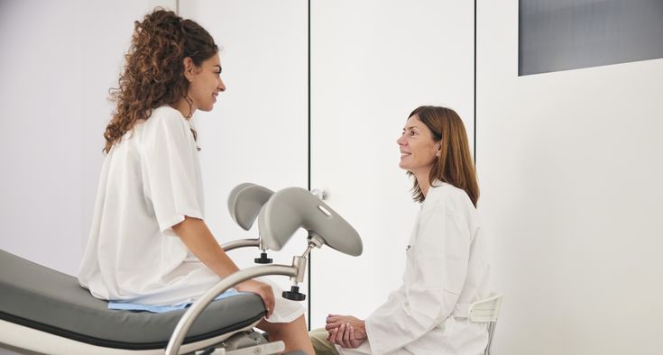 A woman sits on an exam table in a doctor's office and talks with her gynecologist.