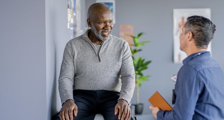 A male patient sits in a doctor's office and talks to his primary care physician.