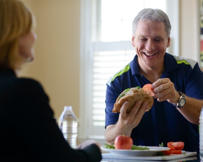 A man smiles while eating a sandwich.