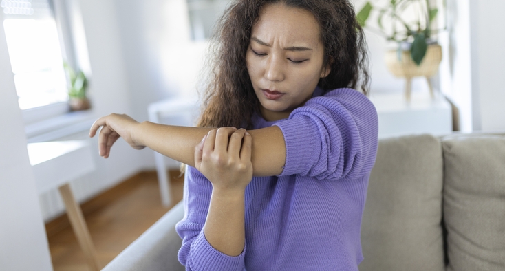 A seated woman grips her elbow and grimaces in discomfort.
