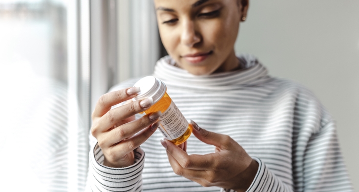 A woman reads the information on a prescription medication bottle.