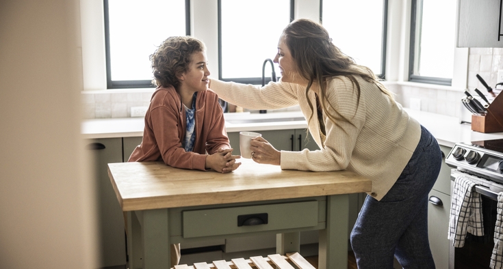 A mom and her adolescent son talk in their kitchen.
