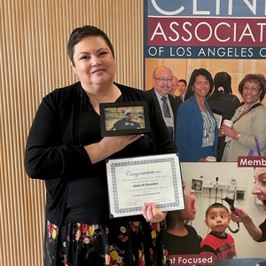 Maria González smiles proudly, holding her graduation certificate and a photo of her son.