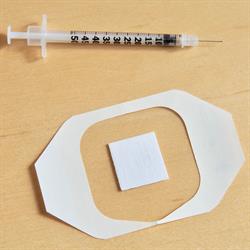 A traditional flu shot is placed above a new needle-free flu vaccine patch.