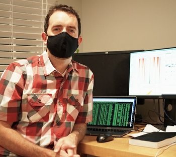 Patrick Murphy, Ph.D., wears a mask and sits next to a computer showing his research results.