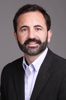 head and shoulders picture of Edmund Lalor. He has short dark brown hair and a short beard with a slight smile showing some teeth. He is wearing a dark grey blazer striped blazer with a light purple button up shirt underneath.