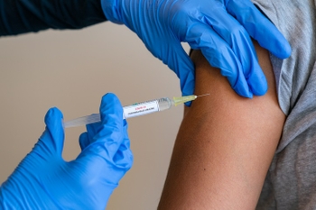 Female doctor wearing blue latex gloves injecting a child in her arm with a needle and syringe containing a dose of the COVID-19 vaccine cure by way of immunisation - 052