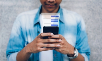 The hands of a young man in a light blue shirt holding a mobile phone and texting