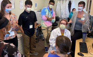 Five students stand around a nurse practitioner and interpreters having a conversation. 