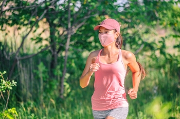 Masked woman jogging in summer park wearing a pink tank top.