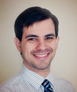 Head and shoulders picuter of Carlos Diaz-Balzac he has brown hair that is combed a short beard and is smiling. He is wearing a striped blue and white buttoned-up shirt with a tie.