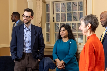 Two men stand on either side of two women talking in a ballroom, they are all smiling.