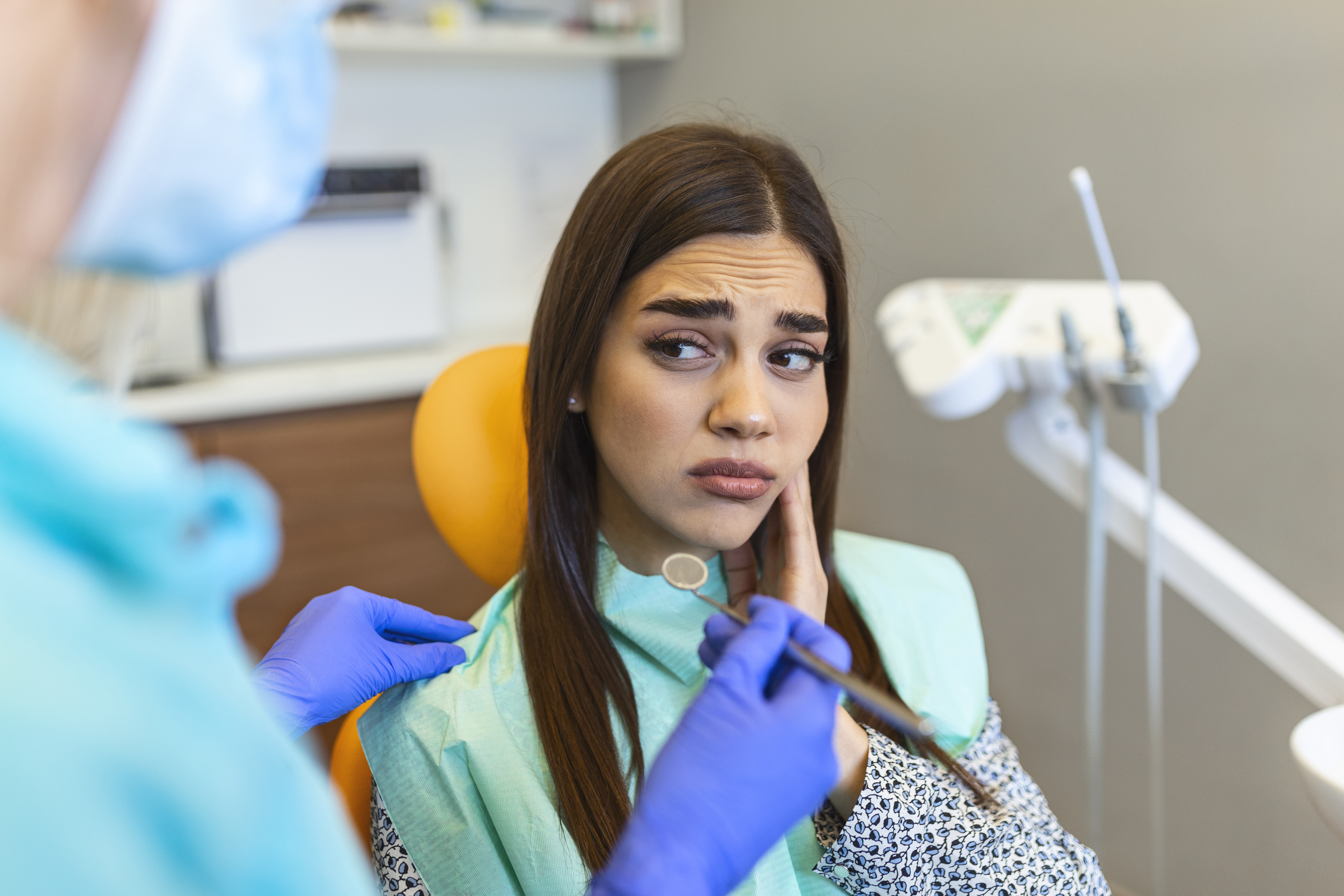 Woman seated in dental chair holding face because she's in pain