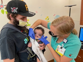 Dr. Shope placing the NAM in baby's mouth while Dad holds him and looks on.