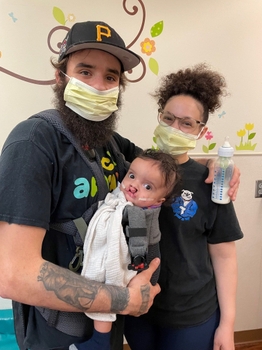 Baby Freddie is held by Dad, with Mom standing next to them