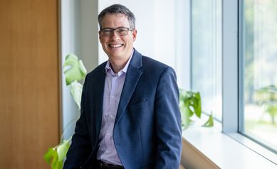 Chad Heatwole, MD, smiling wearing a blue blazer and glasses in front of a wooden frames window and green plant.