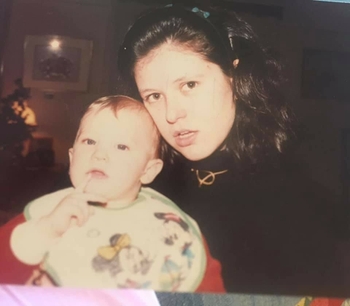 A woman stands next to an infant who is in a high chair