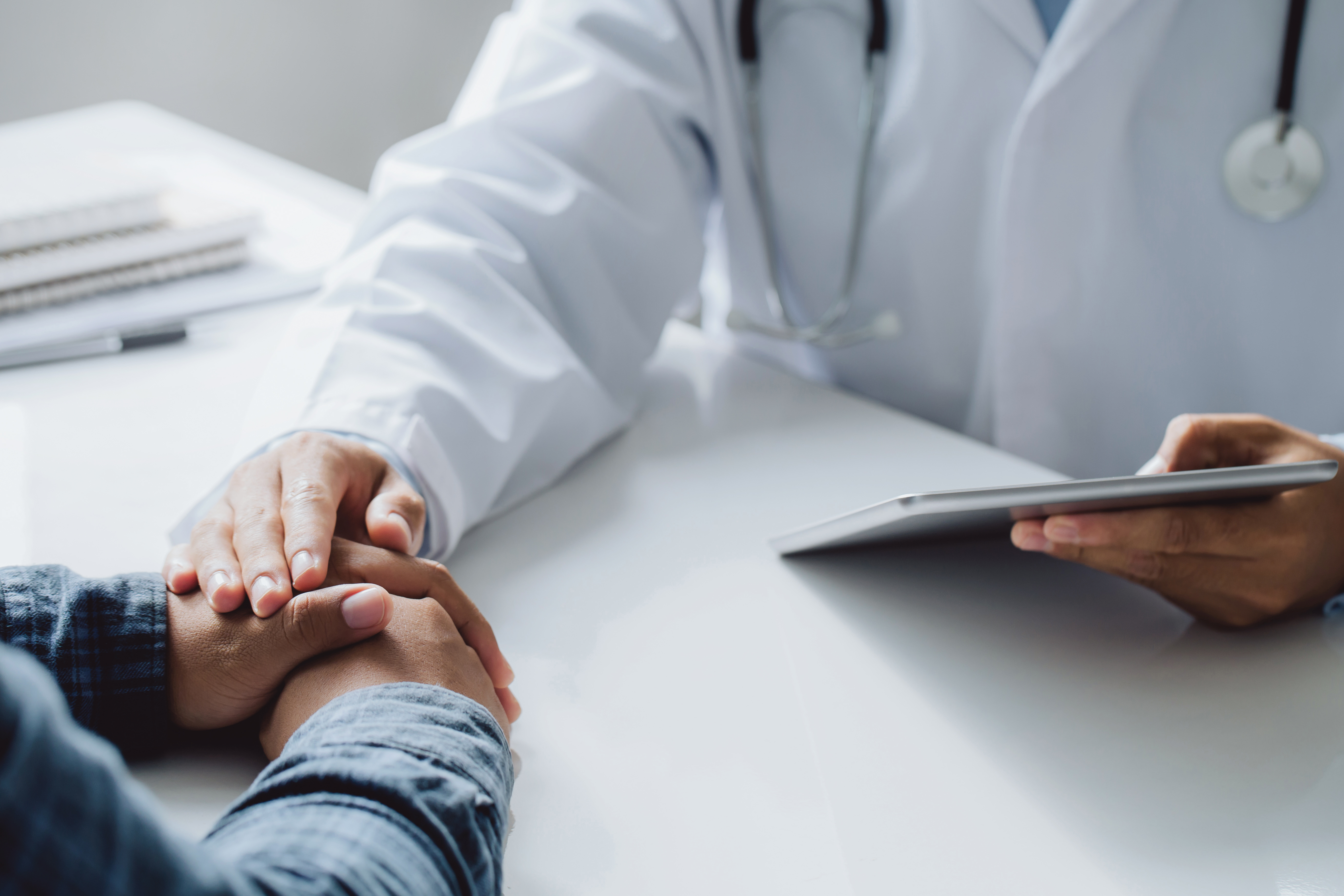 doctor's arm and hand reaching over to comfort patient by touching patient's hand