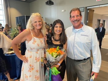Joe and Karen Ferrari stand on either side of Dr. Radhika Thakkar, who holds flowers. All three have big smiles.