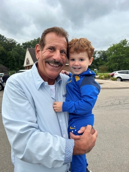 Joe Ferrari holds a small boy, his grandson Arlo. Both are smiling very happily.