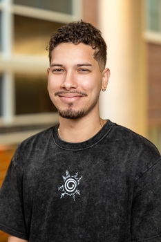 Head and shoulders photograph. John Gonzalez-Amoretti has a short trimmed beard with short dark curly hair. He is smiling and wearing a dark grey shirt,.