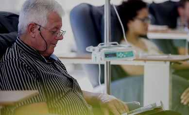 Senior patient receiving treatment while sitting and reading book in hospital ward