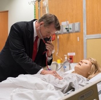 White man wearing suit using a stethoscope to examine a mannequin