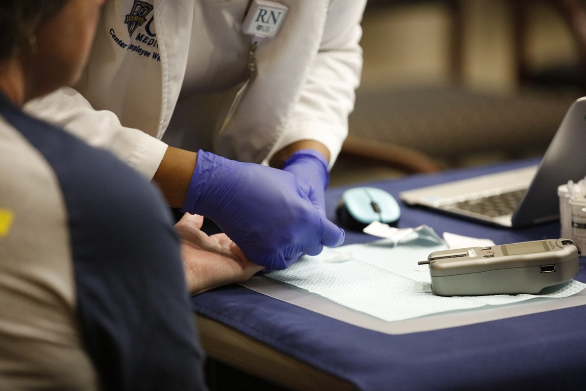 Close-up of a nurse in blue gloves conducting a finger-prick test with a patient.