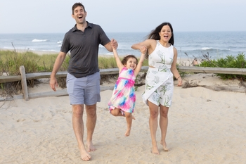 A man and a woman stand on the beach, and swing a happy little girl into the air between them.