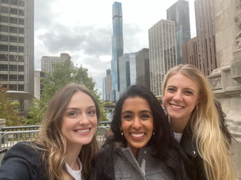 Three women stand in front of a city with tall buildings