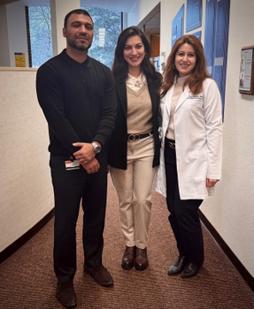 A woman in a suit jacket stands next to a man in black clothing and a woman in a lab coat.