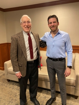 Two men stand together in professional attire.