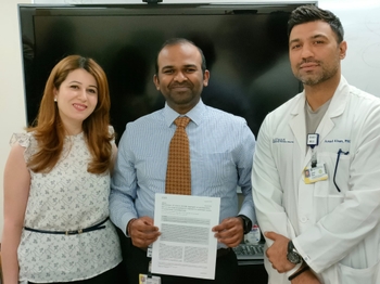 A man in a tie holds a scientific paper. A woman stands to his right and a man in a lab coat stands to his left.