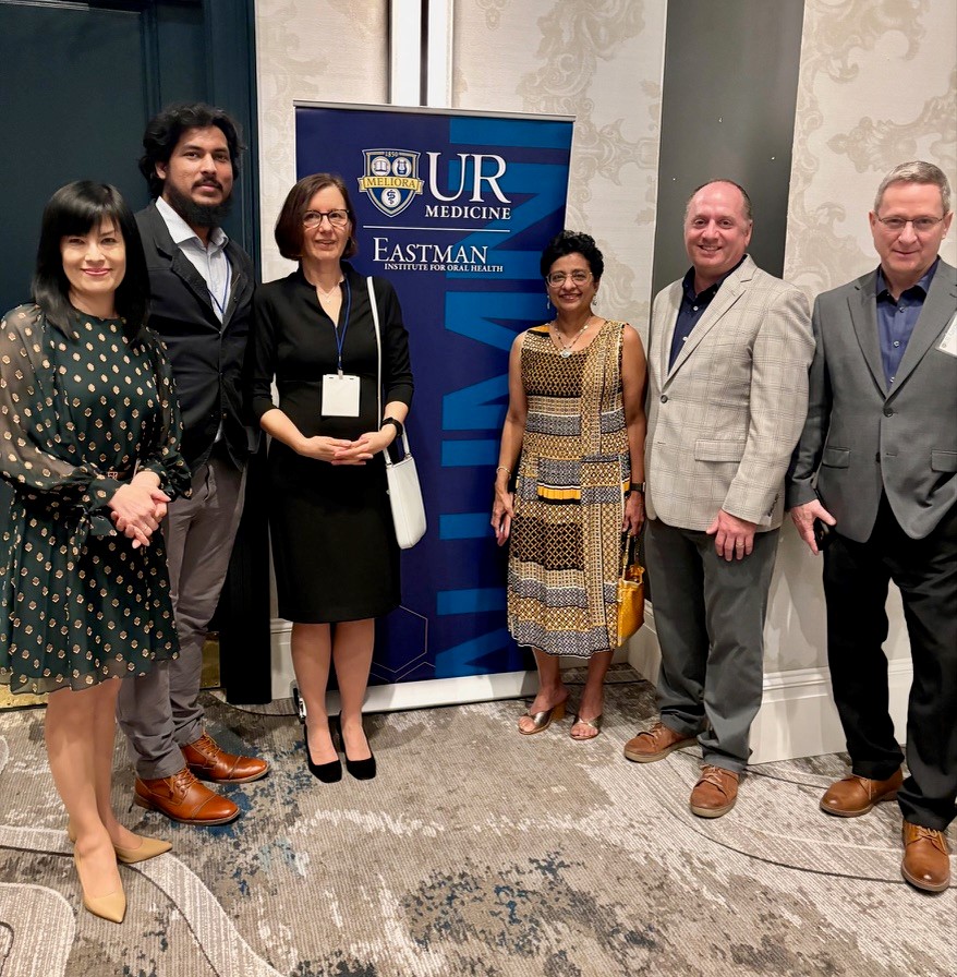 6 people in professional attire stand next to a tall blue sign that reads "UR Medicine Eastman Institute for Oral Health"