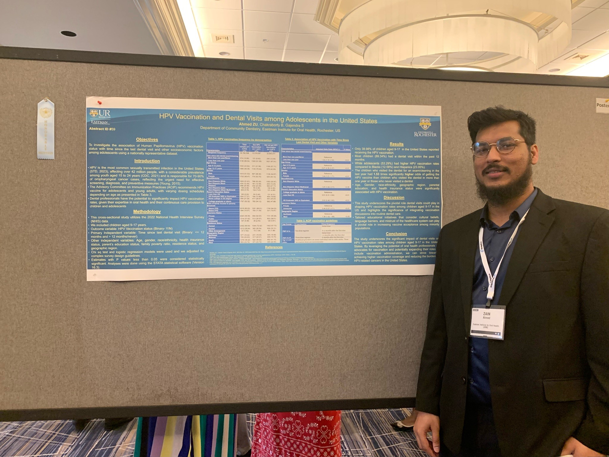 A man in a black suit stands next to a scientific poster. A small white ribbon is hung on the side which reads "Honorable Mention"