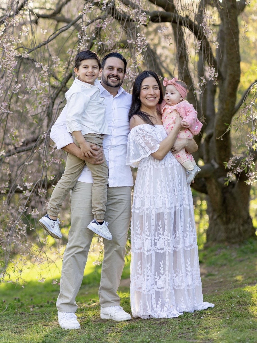 A man and woman hold a young boy and a baby girl underneath a tree with pink flowers.