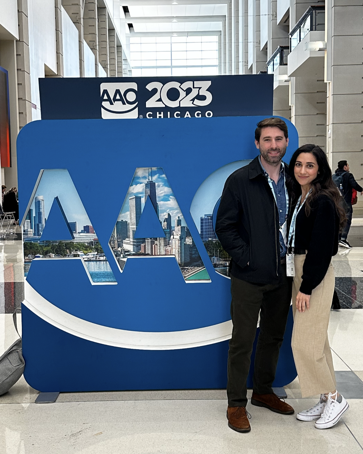 A man and a woman stand in front of a large sign that reads "AAO 2023 Chicago"
