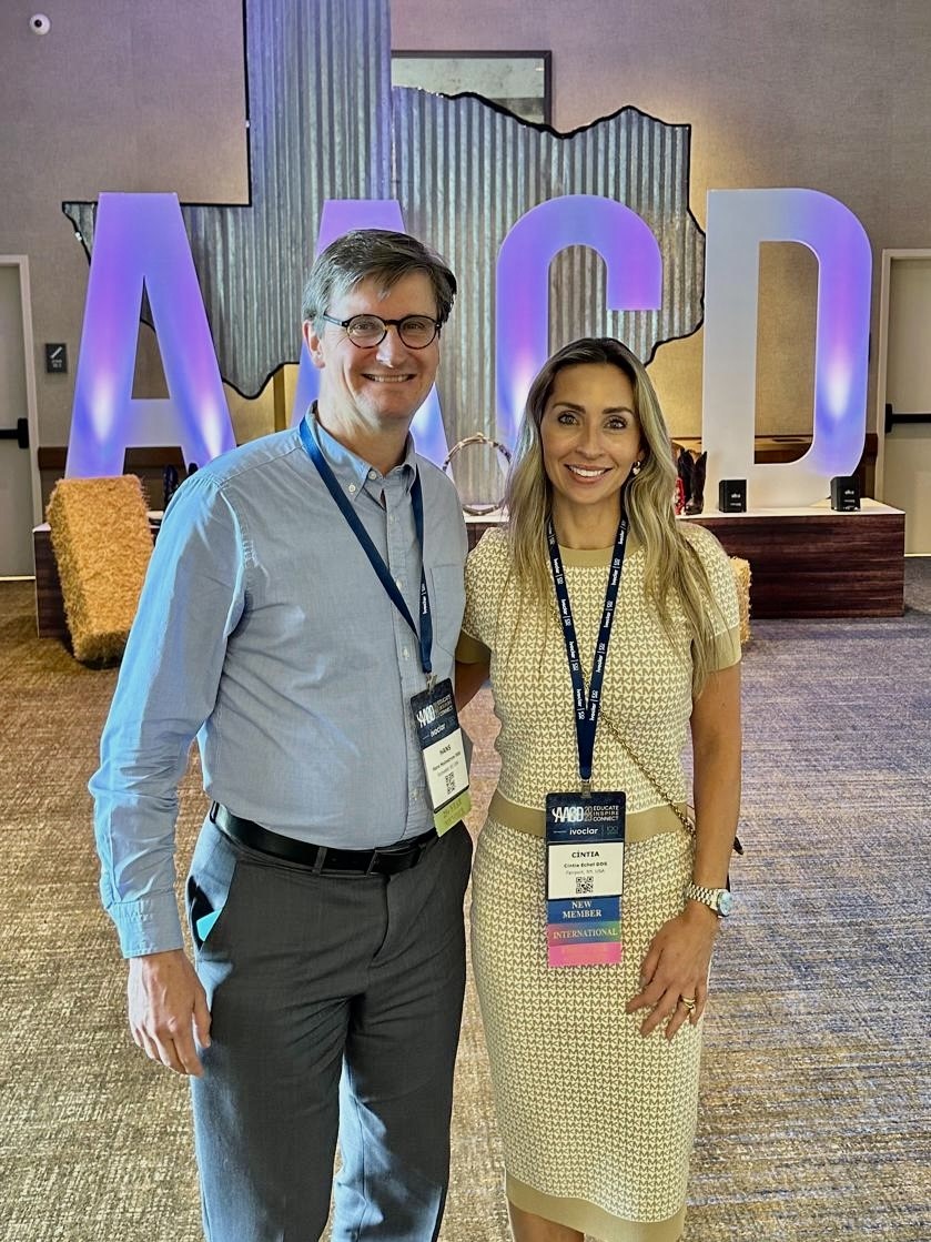 two people stand in front of a sign shaped like Texas with the letters AACD on it.