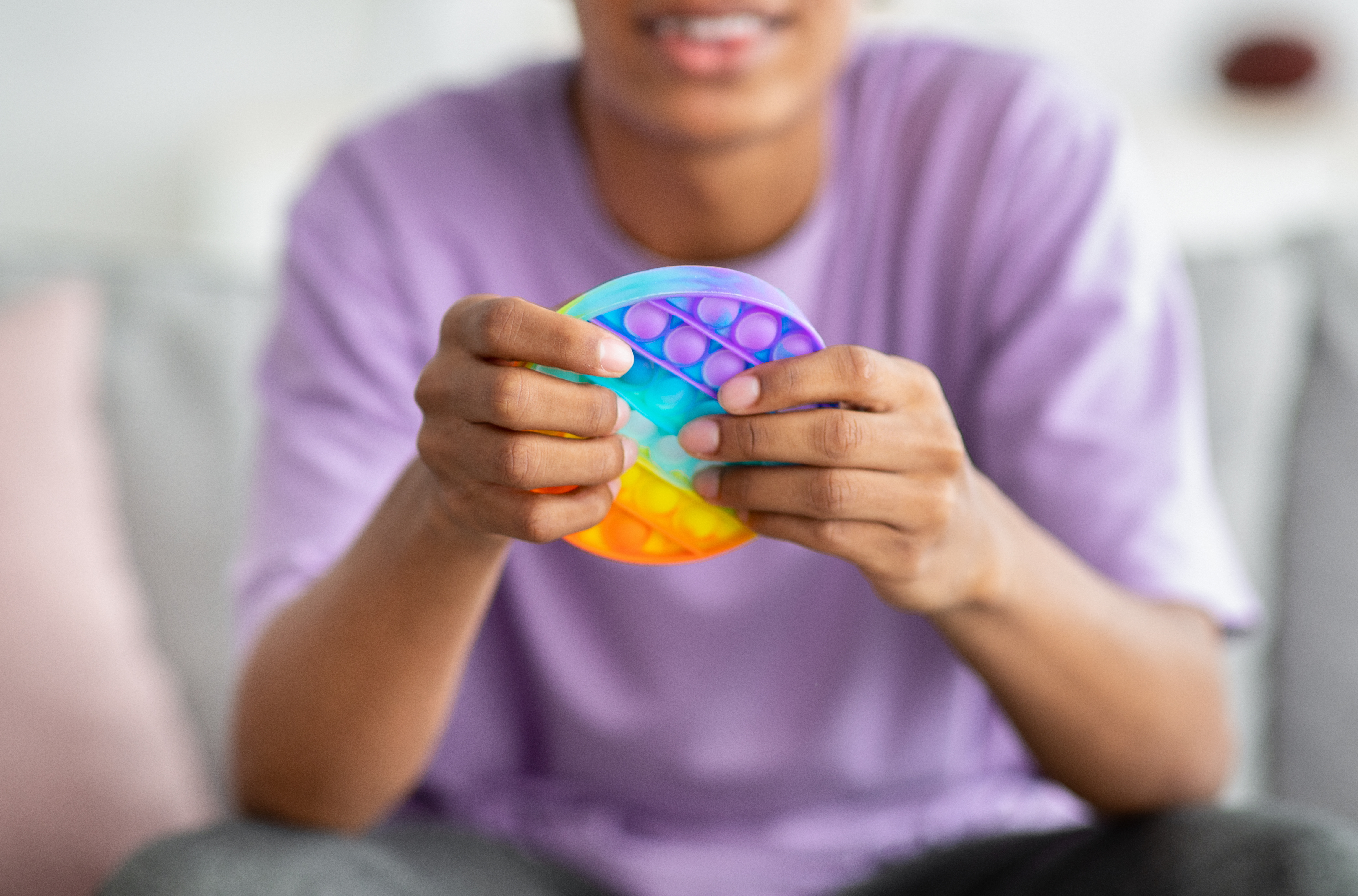 A person in a purple shirt uses a rainbow fidget toy