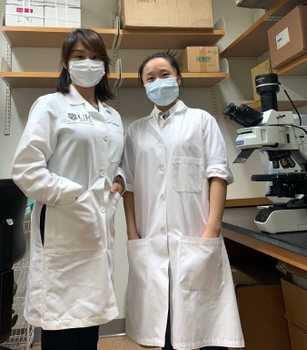 Two people in lab coats next to a microscope